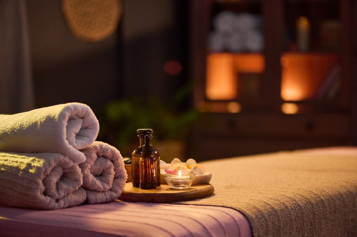 A wellness treatment table with rolled towels, aromatic oil, and soft candlelight